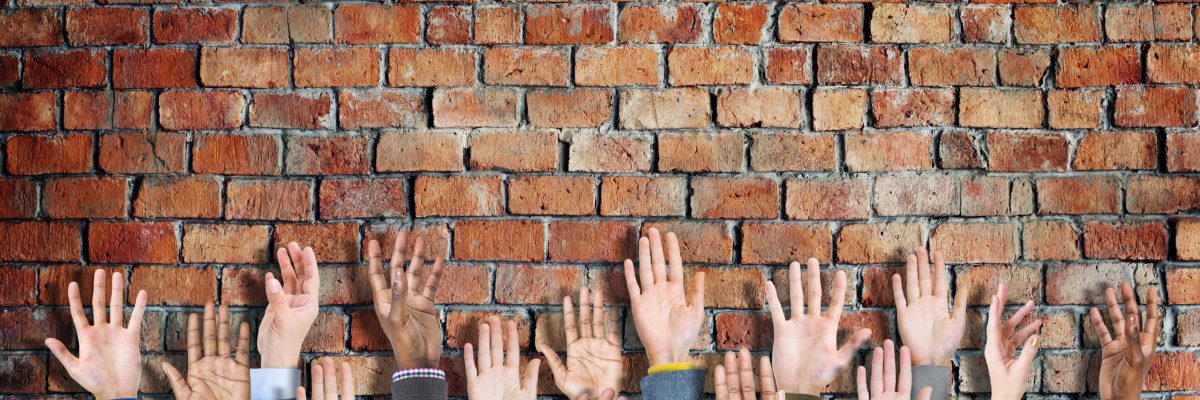 Group of Diverse Casual People's Hands Raised Concept Diverse group on hands raised. Brick wall in background.