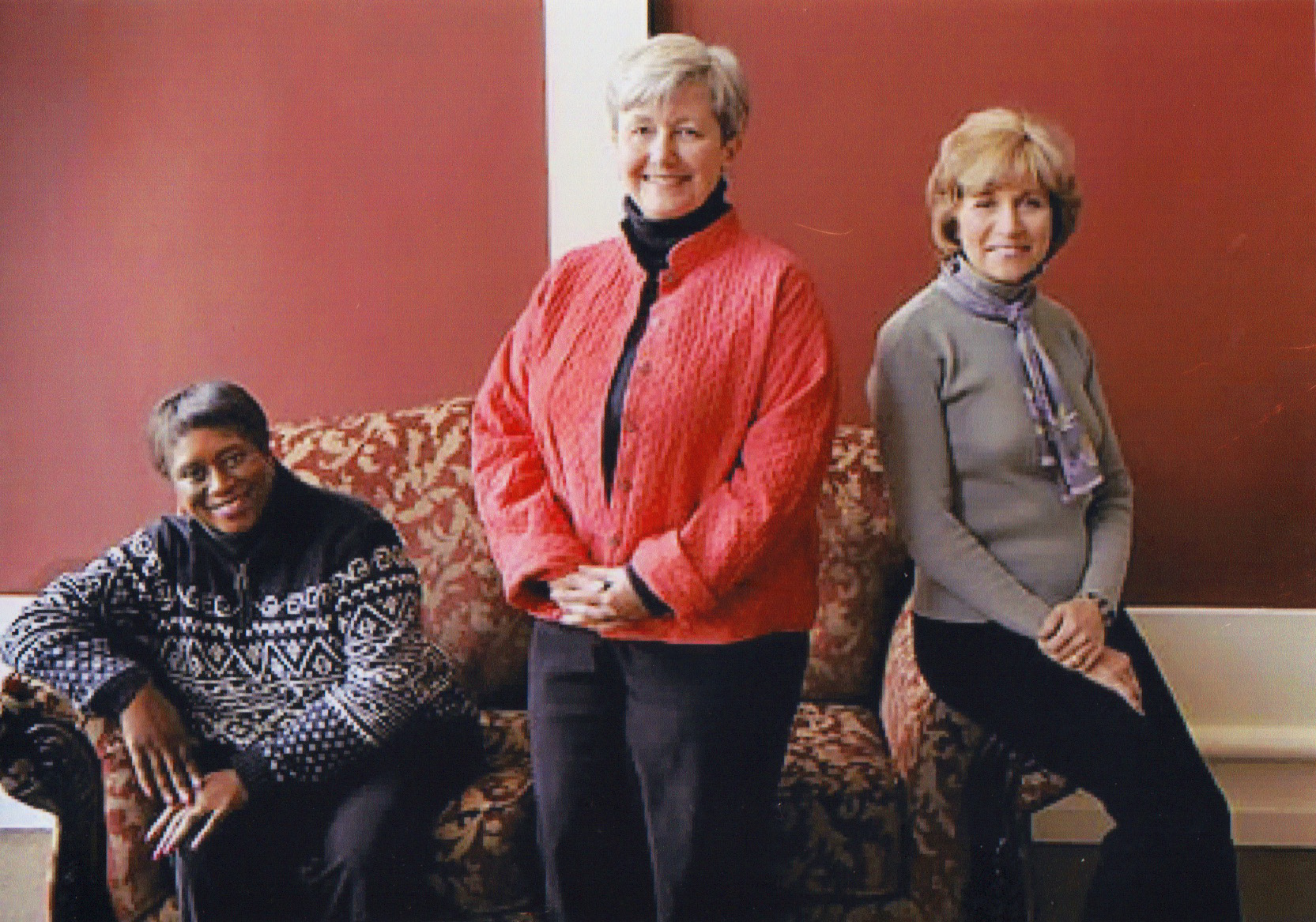 pealfounders Three smiling women posed in front of a sofa.