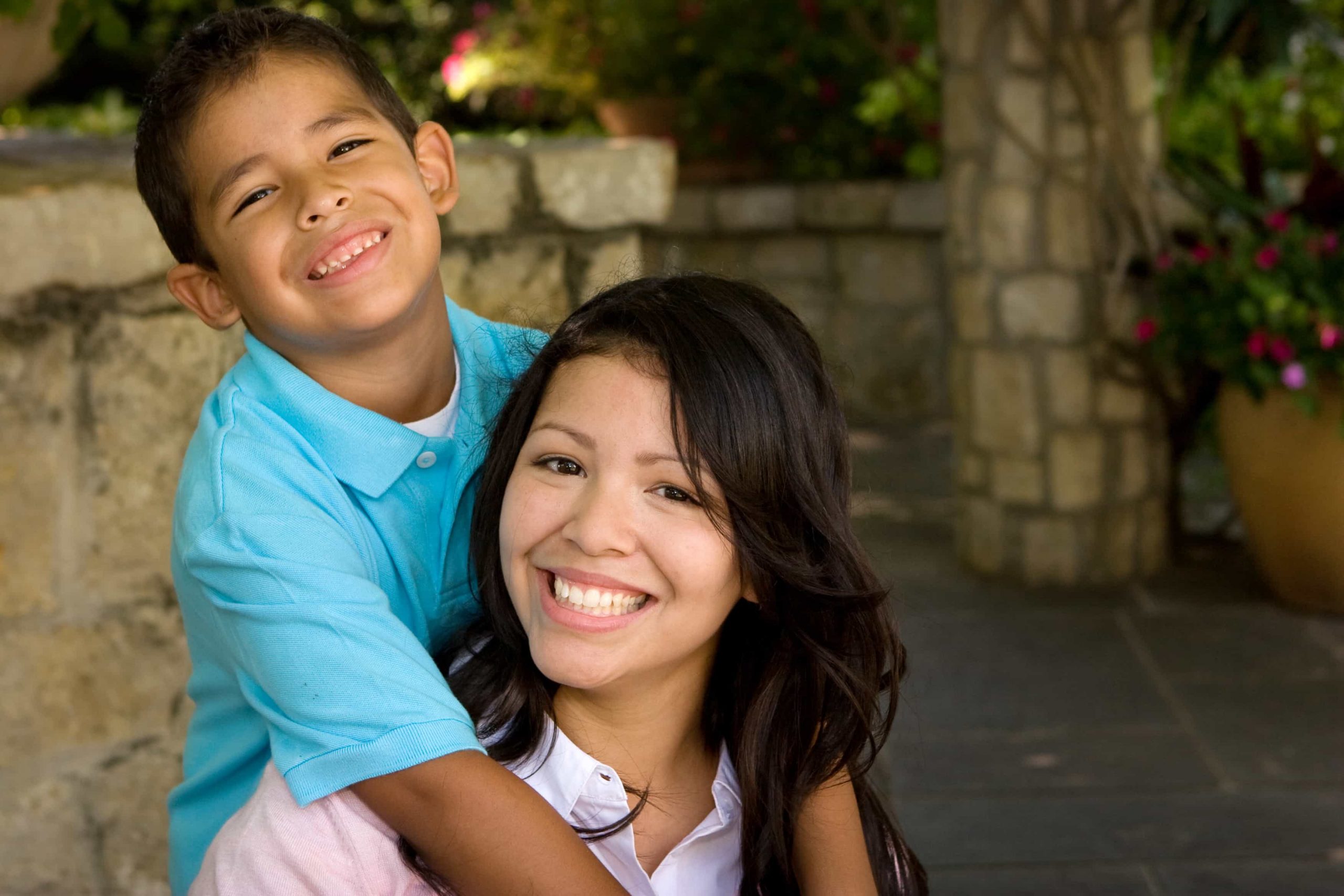 Happy Hispanic mother and her son. Smiling mother sitting, with her son standing behind her embracing her